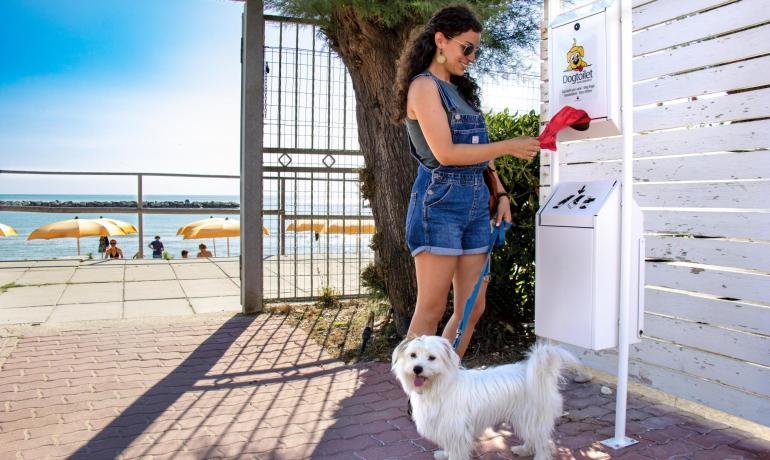 Woman with dog uses bag dispenser at the beach.